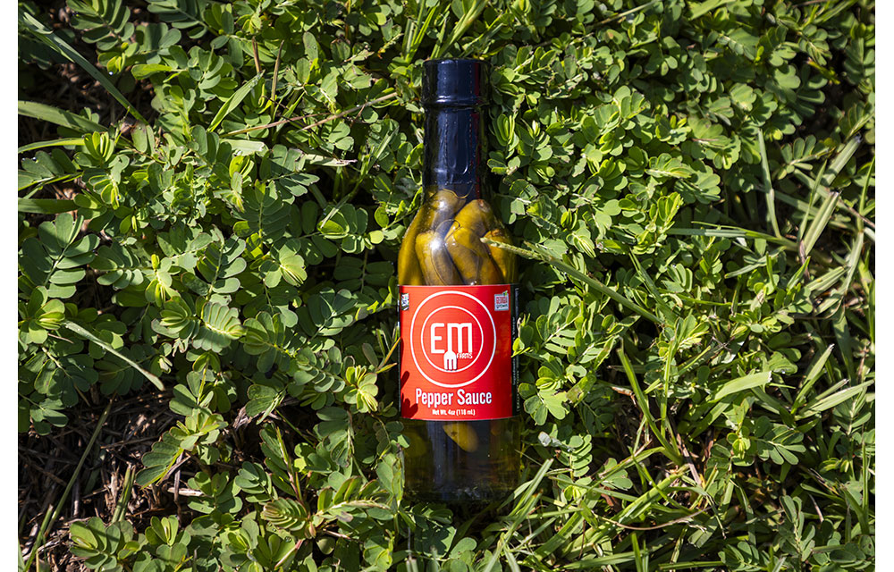 A glass bottle of pepper sauce was sitting in the grass bushes.